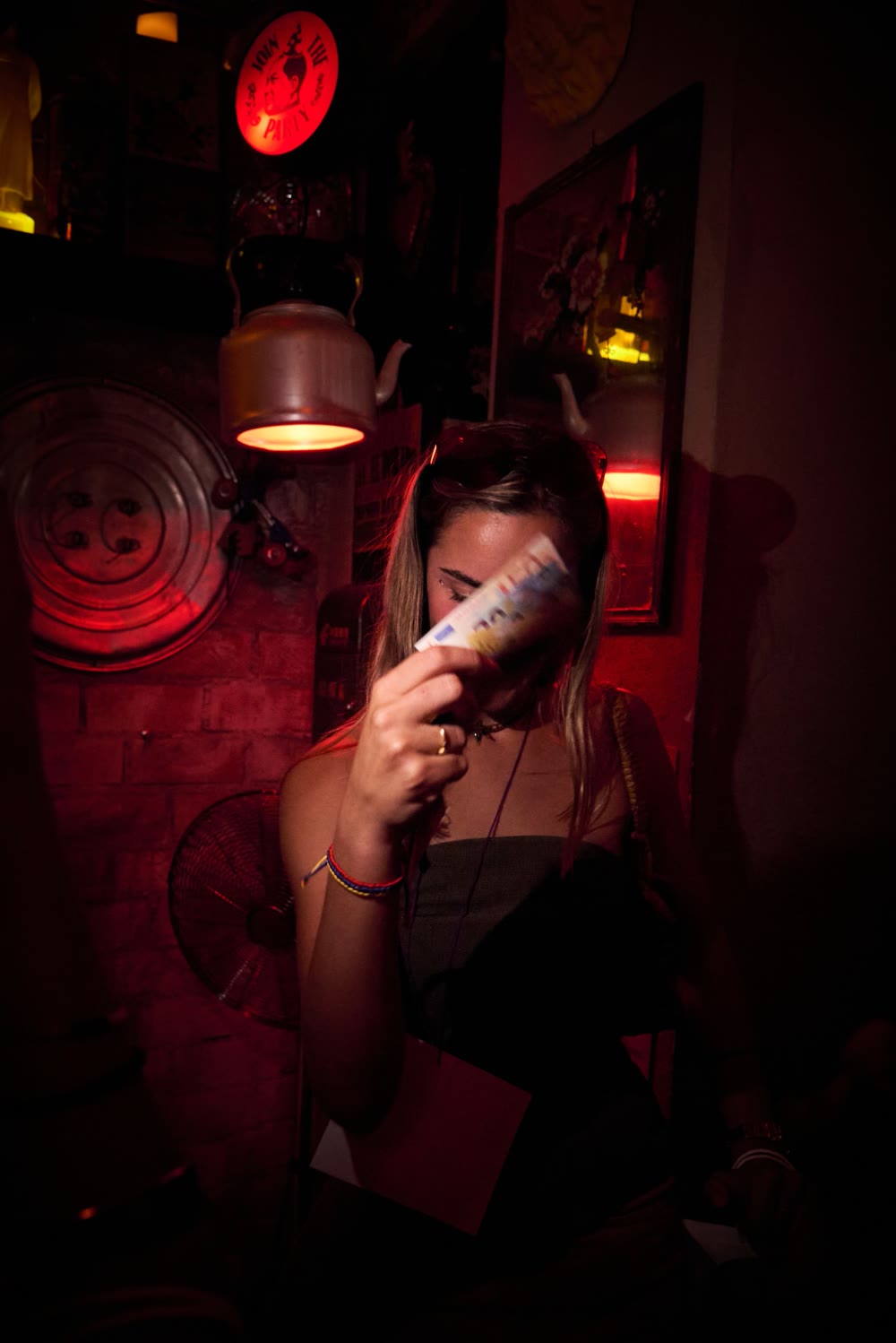 Una invitada bajo luz roja tapándose la cara con un billete